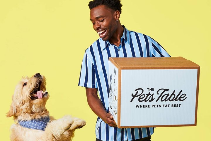 A dog reaching up towards a branded The Pet's Table delivery box